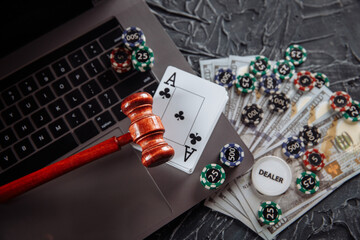 Judge wooden gavel, money banknotes and playing cards on computer keyboard, legal rules for online gambling concept.