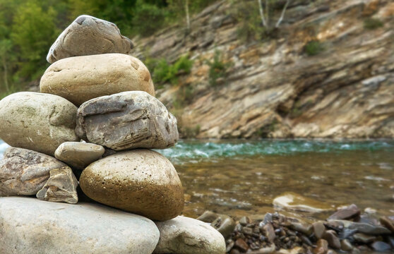 Closeup stone cairn against the background of running water in the river and shore with green grass. Stone balancing along the river. Selective focus.