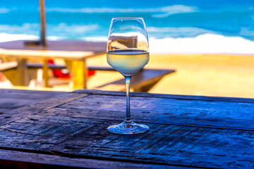 A glass of white wine on wooden table of outdoor restaurant on the beach. Sea view. Summer beach vacation. Hight quality photo