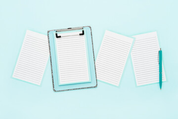 Blank clipboard mockup, empty paper sheets, and ballpoint pen on light blue color background. Top view, copy space. Back to school, deadline, morning concept.