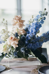 Blue wedding decor. Festive table decorated with flowers on the center, candles, silverware and plates with silk napkins on dusty blue tablecloth