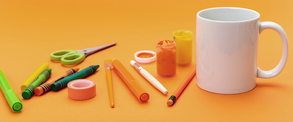 Mug white color and school supplies on orange background. Kids soft drink