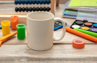Mug white color and school supplies on wooden background. Kids homework soft drink