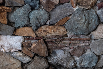 A mosaic of stones and bricks. The wall is made of natural boulders and pebbles. Texture from natural materials. Colorful background. Day Sunny. Georgia.