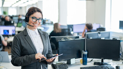 Beautiful caucasian woman in headset is holding a digital tablet while standing in open space...
