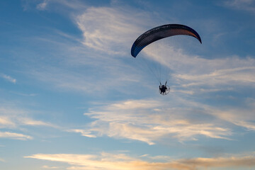 A powered paraglider flying at sunset. Silhouette of moto paraglider (motoparaplan) on a summer sky