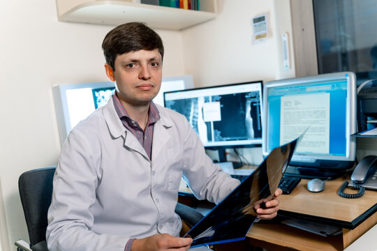 Young male radiologist doctor loking at camera. Computer monitors on the background.