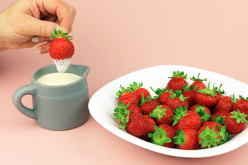 strawberries in a bowl with a hand dipping a strawberry in to a jug of fresh cream.