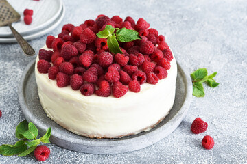 Birthday cake with cream and raspberries on a concrete kitchen background.