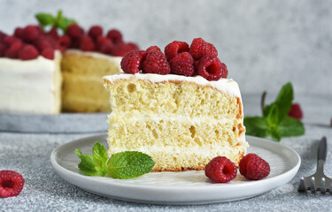 Slice of cake. Birthday cake with cream cheese and raspberries and mint on a concrete kitchen background.