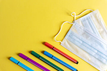 protective mask and school supplies on yellow background, concept of new normality for children and protection against viruses, copy space.Back to school concept