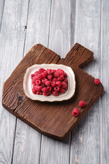 Raspberry fruits in plate on old teak cutting board, healthy pile of summer berries on wooden background, angle view