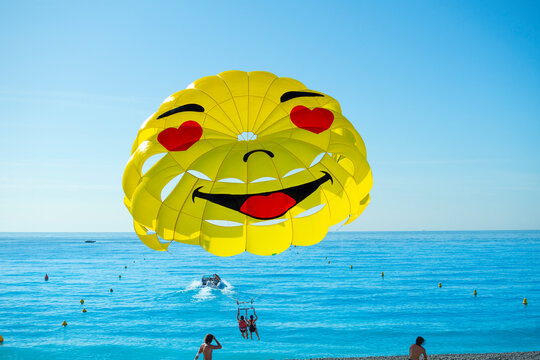 A smiley face parasail parachute takes off from the beach behind a motorboat on the French Riviera in Nice, France