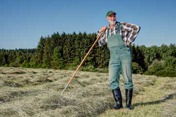 Friendly, smiling ecological farmer stands on his organic hay field in the sun and takes a break from the sweaty hard work... © BIB-Bilder