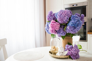 Beautiful pink, blue, purple bouquet of hydrangeas on a gold tray on the table. In the background-the interior of a modern white kitchen in the Scandinavian style. The concept of home comfort.