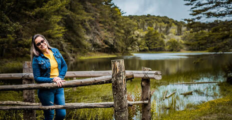 Fototapeta na wymiar Woman smiles at camera in the middle of nature with a lake in the background