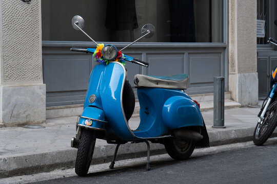 Blue Vespa parked on the street with colorful flowers on the handlebars, vintage scooter