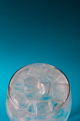 View looking down into a large glass filled with ice cubes set against a teal blue background with copy space available 