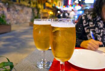 Two beer glasses sit on a table as a woman writes notes at a table of an outdoor cafe in a colorfully lit area of Istanbul, Turkey, at night.