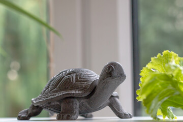 a lazy small brown iron turtle on a white surface in front of a green salad leaf by the window, idea of slow living, slow eating, enjoying countryside lifestyle, keeping artificial animal at home