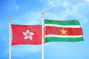 Hong Kong and Suriname two flags on flagpoles and blue cloudy sky