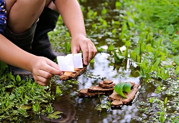 A boy plays with homemade bark boats in a stream after the rain. Children's crafts, creativity....
