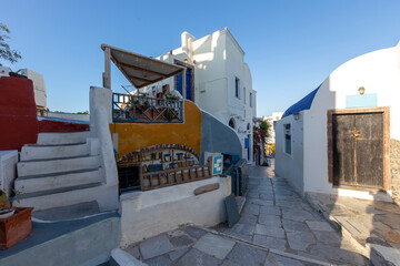 Santorini, Oia, morning dawn in the romantic streets of the fishing village, White and colorful houses built on a cliff above the Caldera, a narrow cobbled street and a beautiful blue sky.