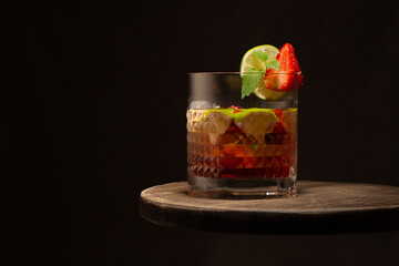 Strawberry and lime coktail in crystal glass with ice cubes and mint leaves on wooden table.Close up.