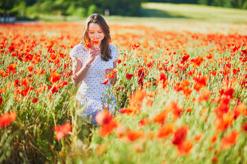 Beautiful young woman in white dress walking in poppy field on a summer day
