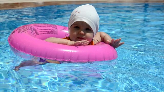 Portrait of happy white Caucasian child baby girl toddler in swimming pool outdoor. Preschool boy training to float with pink inflatable circle ring in water. Healthy active lifestyle. summer, joy