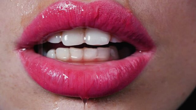 Water drops drip on beautiful female lips, сlose-up. Woman seductively licks her lips with her tongue, beautiful lips and white teeth.