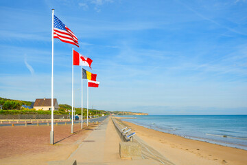 The landing at Normandy coast in France, at Omaha Beach memorial with a row of flags on a sunny day - obrazy, fototapety, plakaty