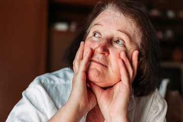 Fototapeta premium Close-up portrait of an elderly woman, hands on her head, looking worried