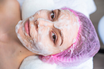 young beautiful girl lies in the spa salon, mask bubbles on her face. self care concept, health, beauty. a pink hat