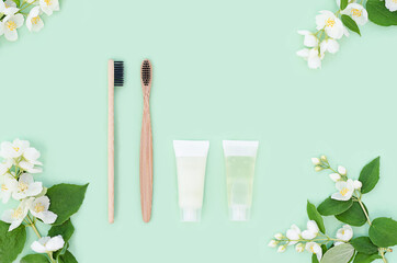 Obraz na płótnie Canvas top view of bathroom accessories, bamboo toothbrushes, natural herbal toothpaste, jasmine branch in eco friendly home on green background. zero waste. copy space, text.