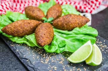 Delicious Lebanese  food, kibbeh (kibe) with sauces and lemon on black slate stone and granite background with traditional keffyeh.