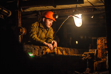 A tired miner in a coal mine looks at the light. Work in a coal mine. Portrait of a miner. Copy...