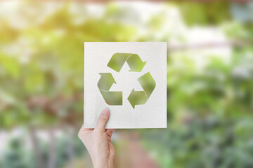 Hand holding cut paper with logo recycle over blur green nature background.