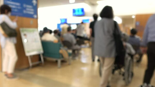 Blurred shot of patients with mask waiting in the crowded lobby at hospital in Japan. Social distancing. 4K