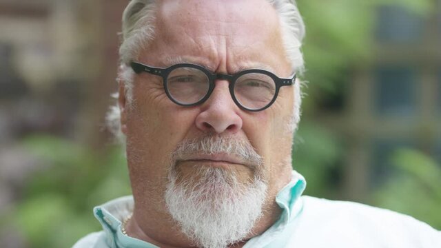 Mature caucasian male looks to camera with a blank expression before smiling