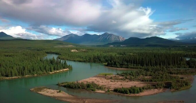 Spectacular countryside scenic flight above Yukon Takhini green river by evergreen tree forest and Mount Ingram mountain range in background on dramatic blue sunny day, Canada, overhead aerial