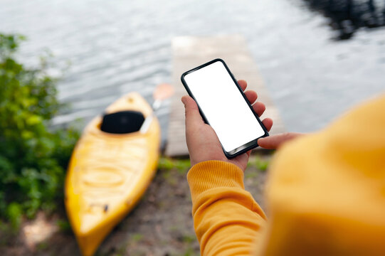 The tourist holds a phone in his hands. Mock up smartphone close-up on the background of a kayak and a lake. Concept on the topic of tourism and recreation.