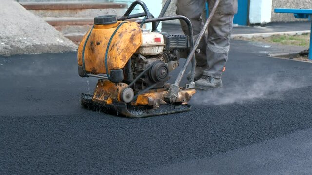 Compaction of asphalt with a road vibroplate. Ramming with your own hands sidewalks near residential buildings.