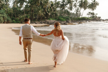 Romantic young just married couple walking together on beautiful exotic tropical beach at sunset