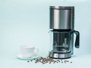 White coffee Cup, coffee maker and scattered coffee beans on a blue background.