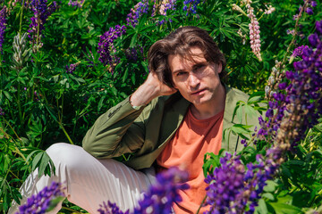 Tall handsome man sitting among the lupine flowers