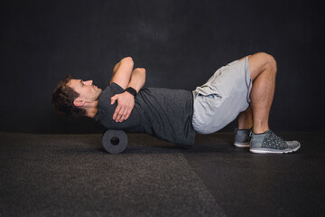 Athletic man using a foam roller to relieve sore muscles and recovers by massaging fascia after a workout.