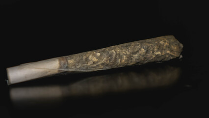 Marijuana tobacco roll with white filter, reflected on a dark surface.