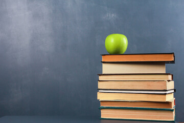 Green apple on stack of books on desk against dark blue wall background. Side view, copy space, close-up, isolated objects. Learning, education, knowledge, library, love reading concept