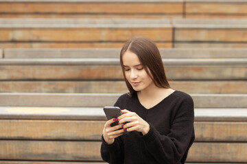 young woman with a phone on the street on a bench smiles